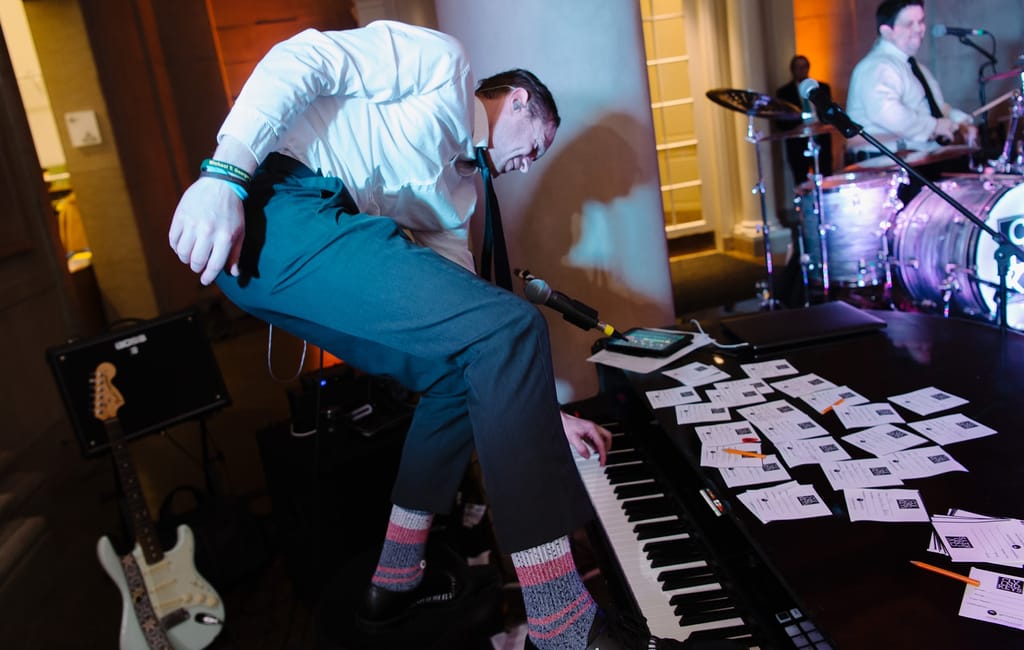 greg standing on piano and playing the piano